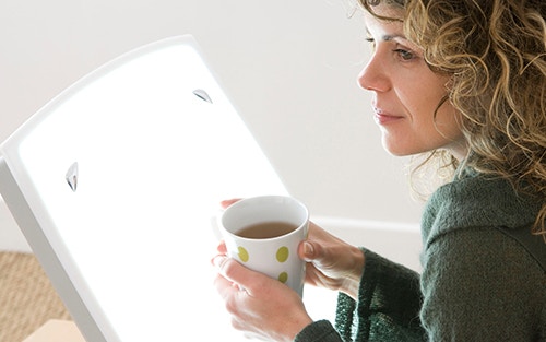 person using light therapy while reading for SAD to improve mood and depression symptoms