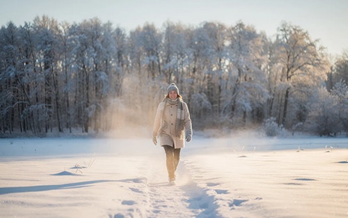 person walking outdoors by snow-covered trees in the bright sunlight, benefits of natural sunlight during winter months